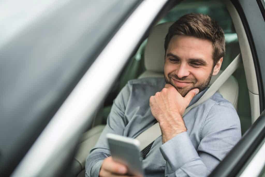 Mann schaut lächelnd auf Smartphone im Auto