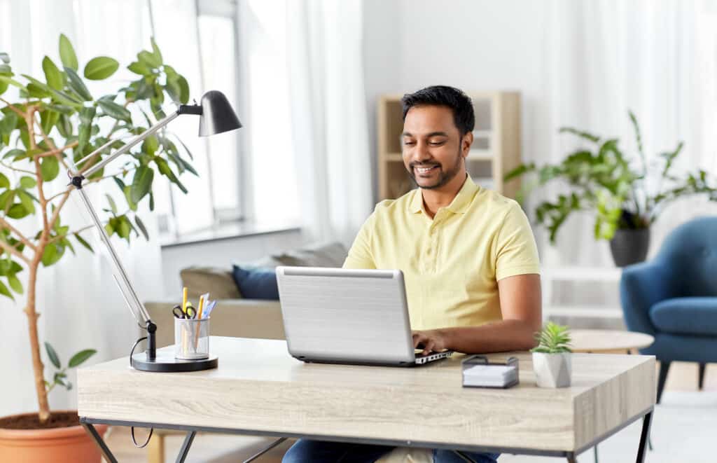 Mann arbeitet lächelnd im Homeoffice am Laptop