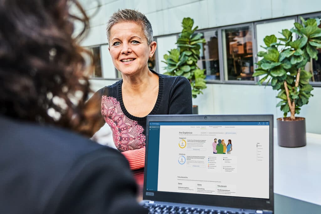 Zwei Personen im Gespräch mit Laptop im Büro.