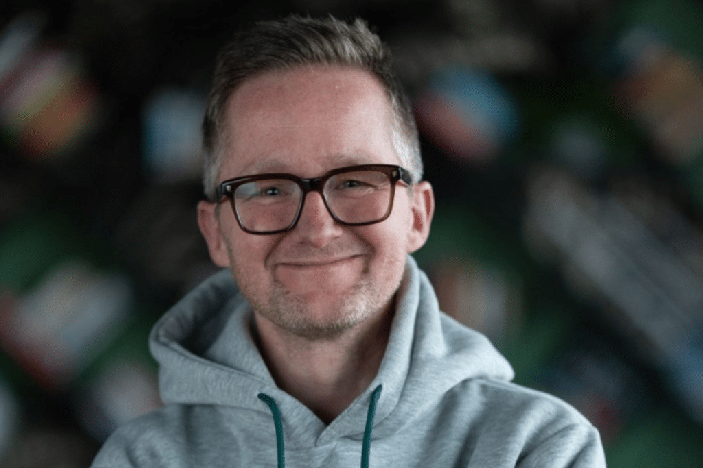 Lächelnde Person mit Brille und grauem Hoodie